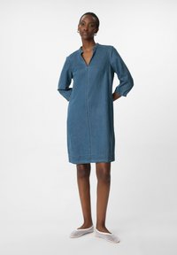 Jeanskleid mit kurzem Kragen, halblangen Ärmeln und geradem Schnitt. Hellblaue Farbe, dezente Nähte und knielanger Schnitt.