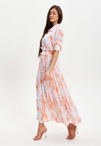 Maxi dress in white with orange watercolor patterns. Features short, rolled sleeves, a ruffled waistband, and tiered skirt.