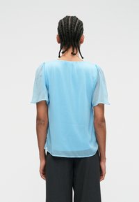 Γαλάζια μπλούζα με κοντά, διάφανα μανίκια και τετράγωνη λαιμόκοψη. Λείο ύφασμα με ελαφριά διαφάνεια και χαλαρή γραμμή.