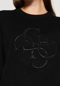 Sudadera negra con un diseño de logotipo texturizado decorado con brillantes strass. La tela es suave y cuenta con un escote tipo crew.