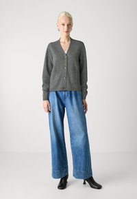 Grå strikket cardigan med V-hals, knappfront og to frontlommer, kombinert med løstsittende lyseblå denimbukser og svarte høye støvler.