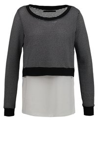 Pull rayé avec un bord noir au niveau de l'encolure et des poignets. La moitié supérieure est rayée noir et blanc, tandis que la moitié inférieure est unie blanche.