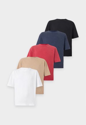 Wysoki mężczyzna w prostym czarnym t-shircie z krótkim rękawem, spodniach moro typu cargo oraz czarnych trampkach, stoi z jedną ręką w kieszeni.