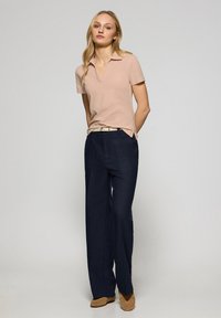 Jasnoróżowa koszulka polo z kołnierzykiem i krótkimi rękawami, w połączeniu z granatowymi szerokimi spodniami i beżowymi balerinkami. Gładki materiał, minimalistyczne akcenty.