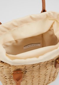 Borsa a spalla intrecciata in paglia con rivestimento color crema, dotata di manici in pelle marrone e un'etichetta con la scritta "TOPSHOP" all'interno.