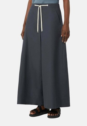 Pantalon gris foncé à jambes larges avec pli devant et cordon blanc, porté avec des sandales noires et un haut bleu, visible de la taille aux pieds.