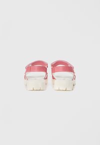 Rosa sandaler med en kraftig hvit såle, med justerbare stropper og en merket bakpanel. Glatt tekstur med minimale designdetaljer.