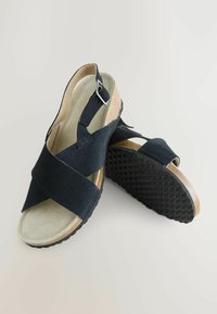 Sandales en suède noir avec des brides entrecroisées, une semelle intérieure rembourrée, une boucle réglable et une semelle en caoutchouc noir texturé.