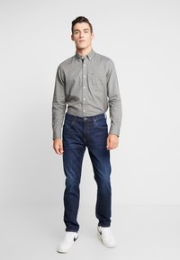 Szary koszula zapinana na guziki z kieszonką na piersi, w połączeniu z ciemnoniebieskimi dżinsami i białymi sneakersami. Prosty design z klasycznym krojem i gładką fakturą.