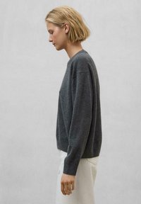Großes, graues Strickpullover mit lässiger Passform, gerippten Bündchen und Saum, strukturiertem Material, gezeigt an einer Person, die seitlich steht.