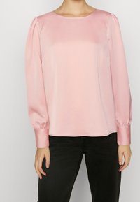 Pink satin blouse with long puff sleeves and a round neckline, featuring smooth texture and subtle sheen. Paired with black pants.
