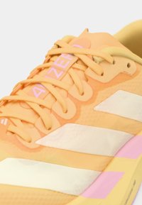 Chaussure de course orange en matériau texturé, avec des accents rose clair, des rayures blanches et des lacets assortis. Dispose d'une semelle amortissante et de détails de marque.