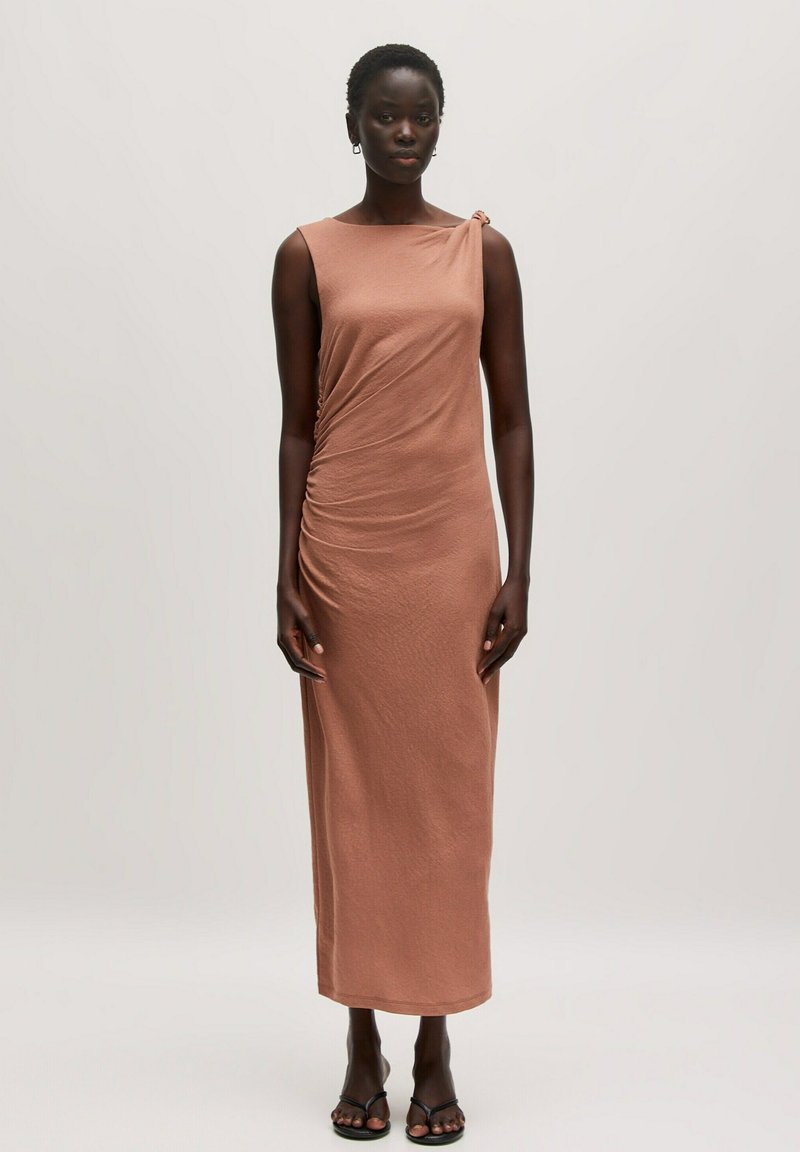 Ärmelloses, rostfarbenes Midi-Kleid mit gerafften Seitendetails und einem Knotenakzent an einer Schulter. Glatter Stoff und figurbetonte Silhouette.