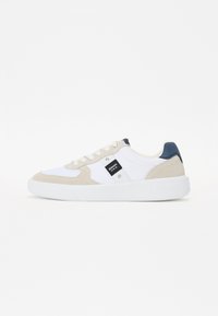 Hvite sneakers med beige semsket skinnaksenter og mørkeblå hæl. Har en teksturert såle og et merket merke på siden.