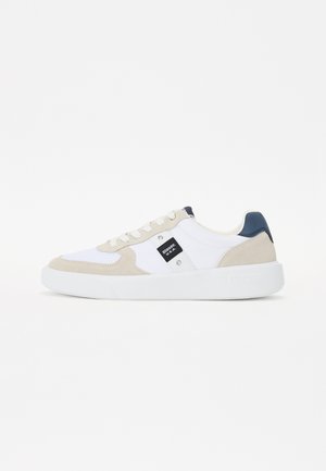 Sneaker bianco con accenti in suede beige e un tallone blu scuro. Presenta una suola testurizzata e un'etichetta con il marchio sul lato.