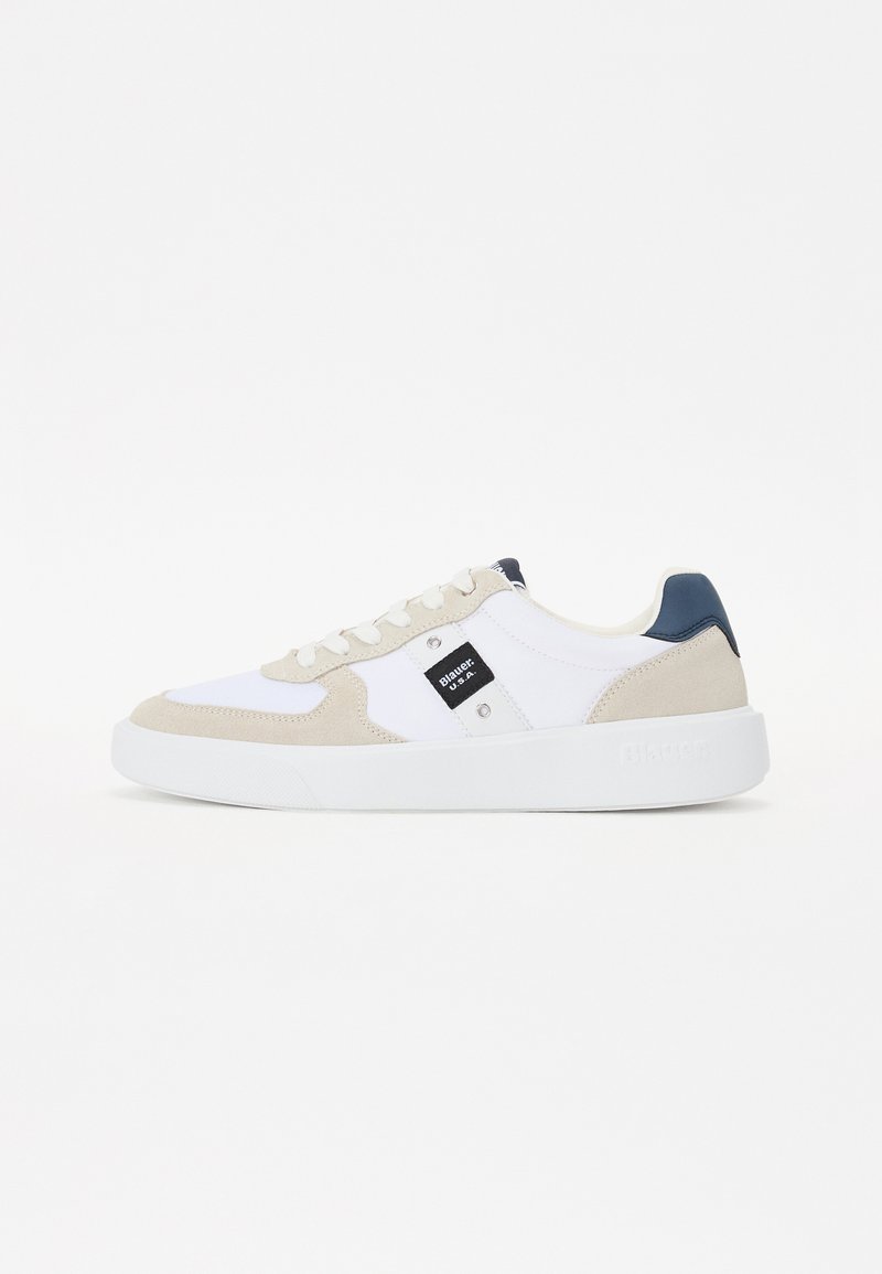 Hvite sneakers med beige semsket skinnaksenter og mørkeblå hæl. Har en teksturert såle og et merket merke på siden.