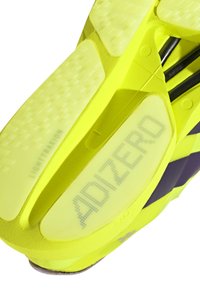 Zbliżenie na jasnorożowo-zieloną podeszwę sportowego buta z brandingiem "ADIZERO" i "LIGHTTRAXION" na teksturowanej powierzchni zapewniającej przyczepność.