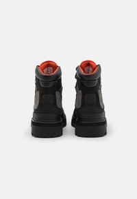 Mustat nilkkurit, joissa on teksturoituja paneeleja, oranssi sisustus, paksut pohjat ja vahvistettu ommel. Sivustoilla metalliseoksia.