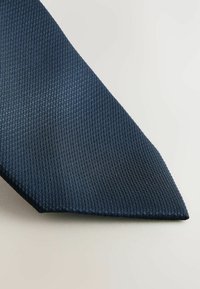 Cravate bleu marine foncé en tissu texturé avec un motif à côtes. L'extrémité étroite présente une pointe sur fond clair.