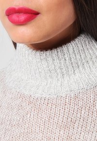 Vaaleanharmaa korkeakauluksinen neulepaita, jossa on ribbineulos ja pehmeä neulospinta. Lähikuva kaula-aukon ja ylärinnan alueelta.