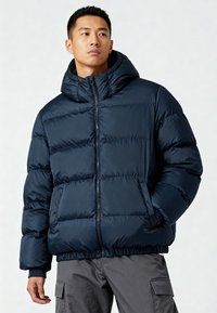 Giacca a vento imbottita blu navy con cappuccio, chiusura con zip e polsini elasticizzati, caratterizzata da un design trapuntato e due tasche laterali.