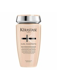 Kérastase Curl Manifesto shampoo in a curved, cream-colored bottle with silver accents. Text indicates hydrating properties for curly hair.