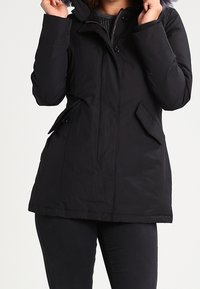 Veste isolée noire avec capuche, dotée de boutons sur le devant, de deux poches latérales et d'une doublure intérieure texturée. Matière lisse et résistante à l'eau.