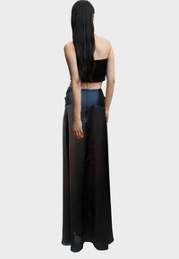 Falda maxi de satén negro con una cintura alta, que presenta una textura suave y un diseño fluido. Combinada con un top corto negro ajustado.