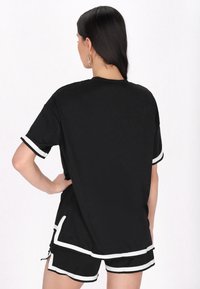 Sort kortærmet top med hvid kant, der har en afslappet pasform. Kombineret med sorte shorts med hvide striber langs kanten.
