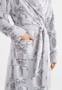 Fleece-Bademantel in Hellgrau mit dezenten Schleifenmustern. Verfügt über einen Bindegürtel, eine Seitentasche und gerippte Bündchen für zusätzlichen Textur.