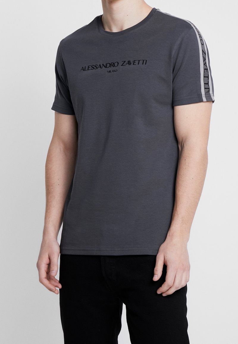 T-shirt en coton gris avec un col rond, des manches courtes et un logo brodé sur la poitrine. Détails de rayures sur les côtés avec des accents de logo.