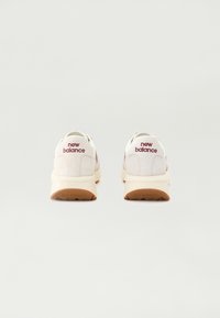 Fehér sportcipők velúr felsőrésszel és bézs kiegészítőkkel, párnázott talppal, valamint bordó színű "new balance" márkajelzéssel a saroknál.