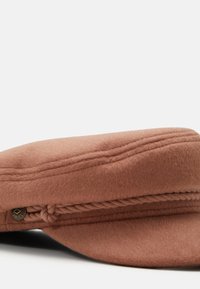 Gorra de lana marrón con coronilla plana, detalle de trenza lateral y acento decorativo de botón metálico. Textura suave y diseño estructurado.