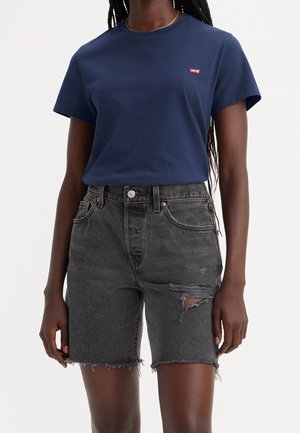 Persona que lleva una camiseta de Levi's azul marino y unos pantalones cortos de mezclilla negros desgastados de talle alto con dobladillos deshilachados.