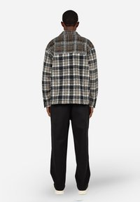 Φόρμα από φλις σε μαύρο, καφέ και άσπρο καρό σχέδιο; χαλαρή εφαρμογή; περιλαμβάνει γιακά και μακριά μανίκια; συνδυάζεται με μαύρους παντελόνες.