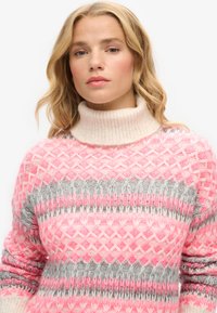Pull en tricot avec un col montant dans des tons de rose clair, rose foncé et des motifs gris, présentant un design en losange texturé et des manches côtelées.