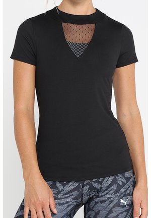 Femme portant un top noir ajusté à manches courtes avec une découpe poitrine en mesh et motif en treillis, et des leggings Puma foncés à motifs.