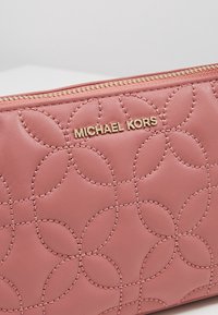 Pochette in pelle rosa di Michael Kors con hardware dorato. Presenta un motivo circolare trapuntato e una chiusura con zip per una sicurezza ottimale.