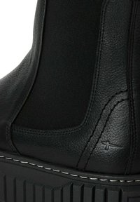 Botín negro hasta el tobillo con parte superior de cuero y tela, con una suela texturizada, costuras blancas contrastantes y un pequeño logo en el lateral.