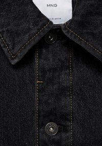 Schwarzes Denim-Hemd mit spitzem Kragen, kupferfarbenen Nähten und einem Metallknopf mit dem Markenlogo. Das Etikett enthält den Markennamen und die Größe.