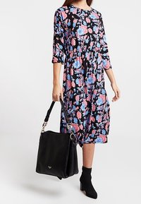 Černé květinové šaty s růžovými a modrými růžemi, s nařaseným pasem, tříčtvrteční rukávy, doplněné černou kabelkou a kotníkovými botami.