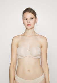 Beige strapless bh laget av glatt stoff med lett polstring, med en liten sløyfe i midten og delikat bølget kant rundt kantene.