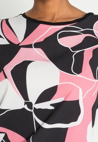 Maglietta a maniche corte con scollo rotondo, caratterizzata da un audace motivo floreale in rosa, nero e bianco su uno sfondo in tessuto liscio.