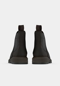 Schwarze Leder-Boots bis zum Knöchel mit elastischen Seitenpaneelen und Zuglaschen, ausgestattet mit einer stabilen Gummisohle und einer glatten, matten Oberfläche.