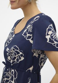 Marinblå klänning med korta ärmar, prydd med vita blommönster, V-ringning och en figurnära midja med knytaccent. Slät tygtextur.