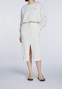 Sweat-shirt blanc à épaules tombantes, associé à une jupe longueur genou avec une fente à l'avant. Les deux sont fabriqués en tissu doux et texturé.