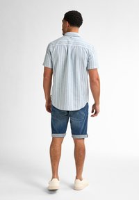 Lichtblauw gestreept overhemd met korte mouwen en een gebogen zoom, gecombineerd met opgerolde denim shorts. Schoenen zijn lichtgekleurde sneakers.
