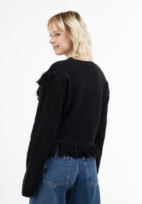 Pulover negru cu mâneci lungi, țesătură texturată și margine franjurată. Asortat cu blugi blue high-waisted, evidențiind o croială lejeră.