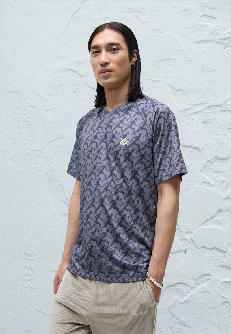 Šedé tričko so vzorom a jemným motívom vtáka, výstrih do V, krátke rukávy a malý logotyp pri hrudi.