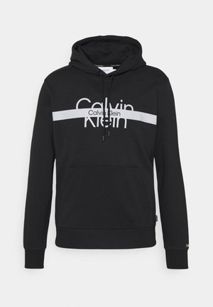 Sort hættetrøje med frontlomme, hvid vandret stribe og "Calvin Klein"-logo tværs over brystet.